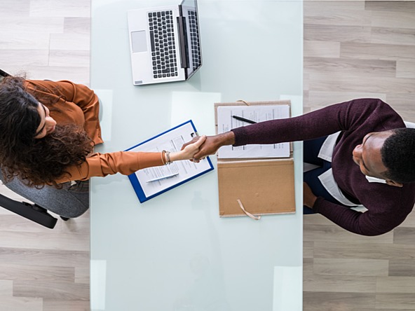 overhead view of man and woman shaking hands across a desk during interview